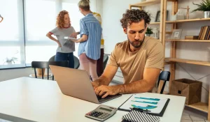 Man working on laptop with colleagues in background