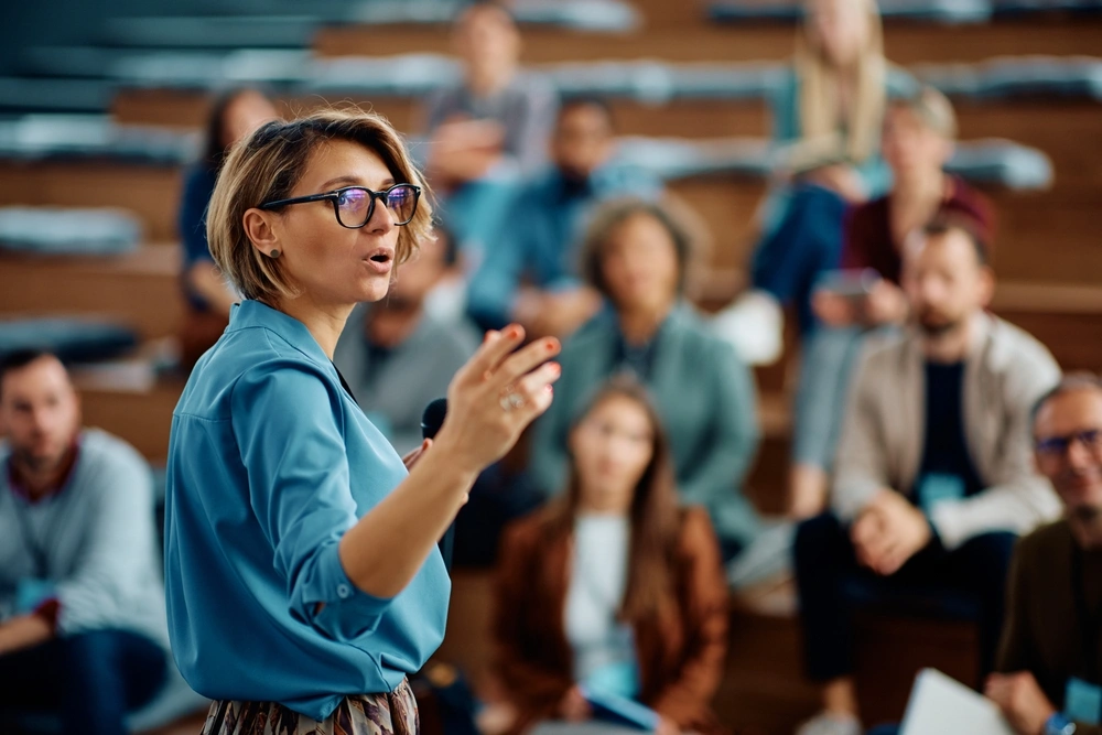 Woman speaking to audience in lecture setting.